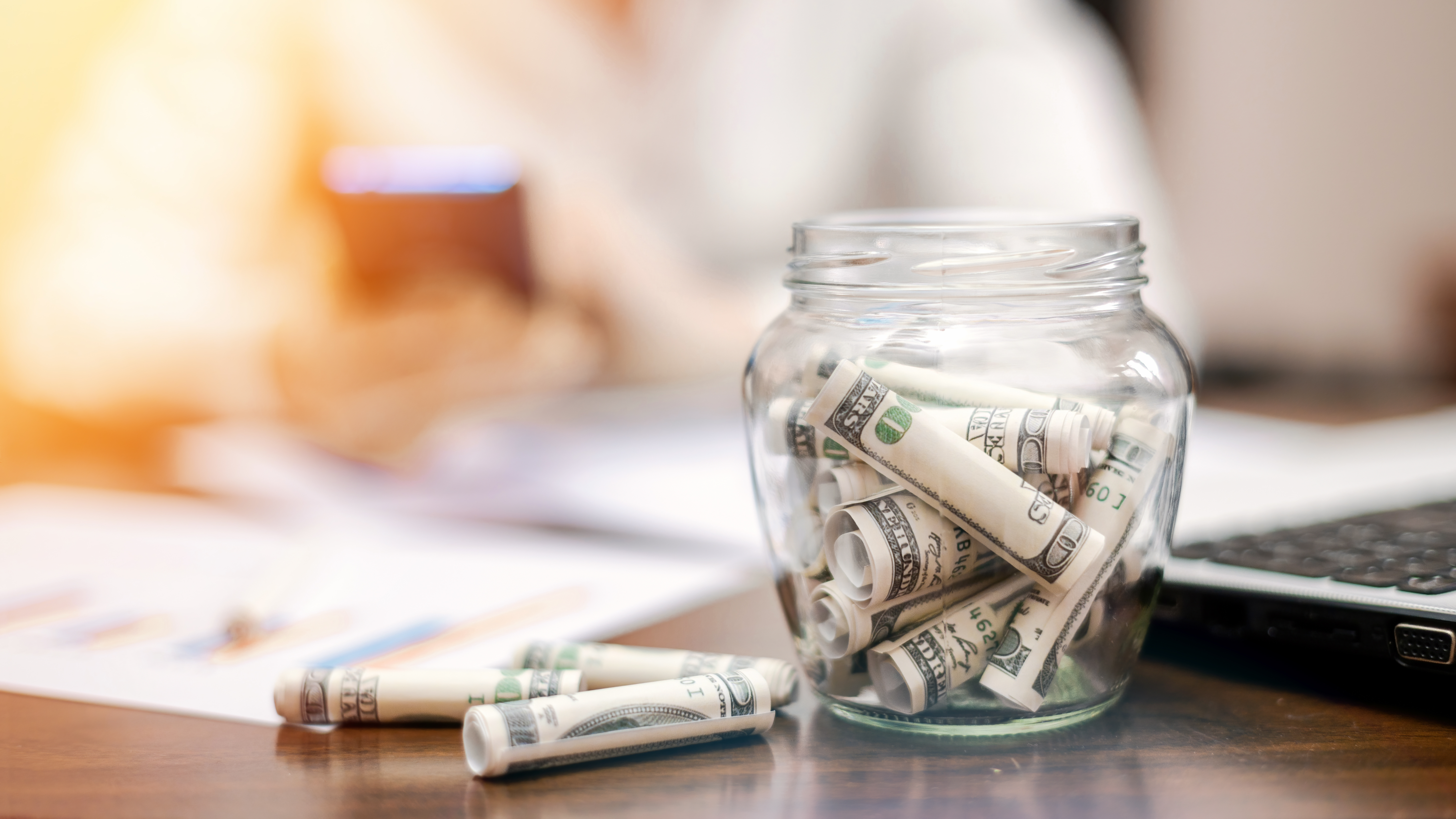 jar-with-rolled-banknotes-table-laptop-papers-woman